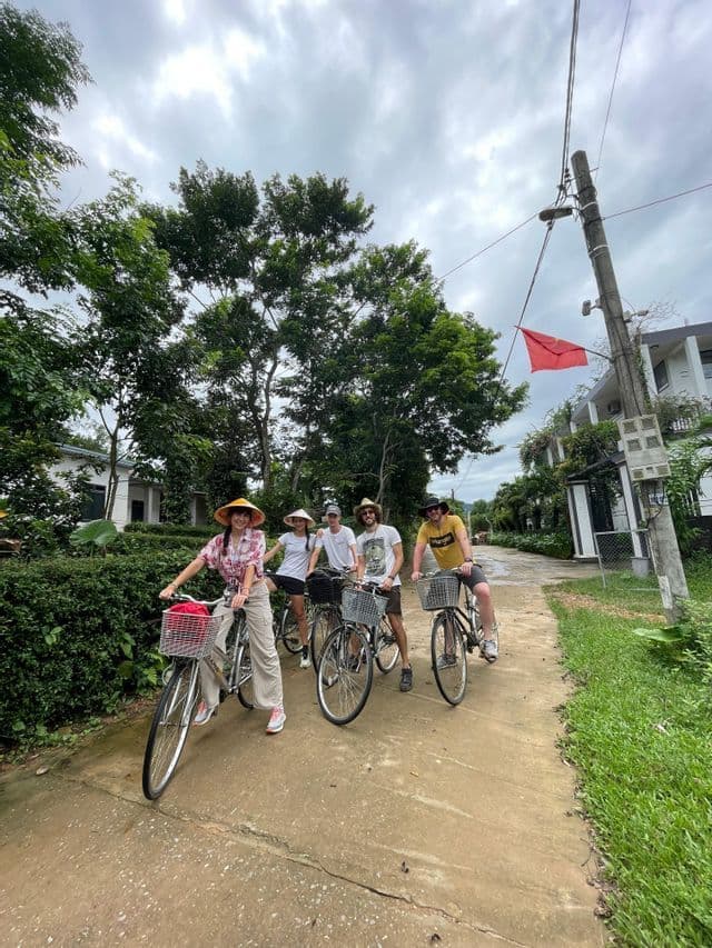 Un viaggio di gruppo WeRoad di cinque persone in posa sulle loro biciclette su un sentiero rurale circondato da alberi rigogliosi sotto un cielo nuvoloso.