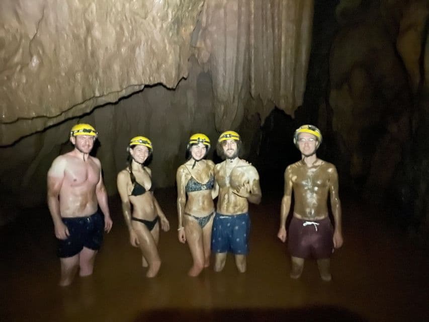 Cinque persone di un gruppo WeRoad, coperte di fango, con caschi, immerse nell'acqua fino alla vita all'interno di una grotta.