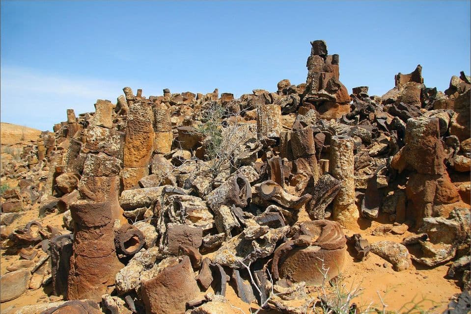Una distesa di formazioni rocciose colonnari bruno-rossastre, sparse su un pendio sabbioso sotto un cielo azzurro e limpido.