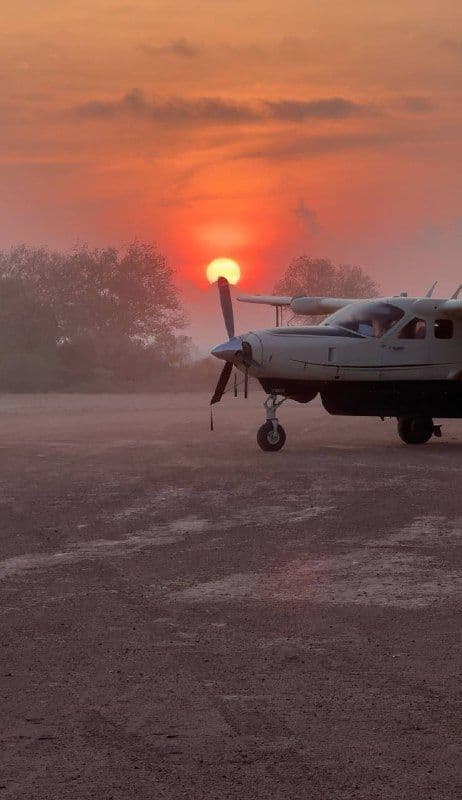 Un piccolo aereo ad elica parcheggiato su un campo polveroso al tramonto, con il sole arancione che splende dietro la sua elica.
