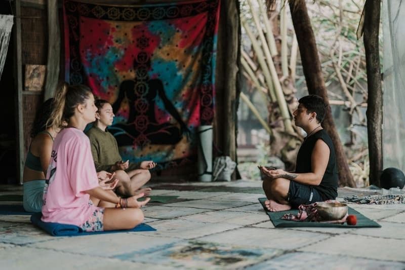 Un voyage de groupe WeRoad méditant sur des tapis dans un studio rustique, face à un instructeur en position du lotus.