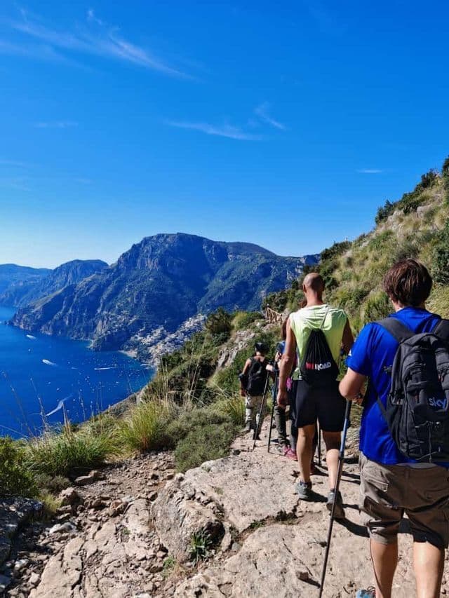 Un viaggio di gruppo WeRoad con trekking su un sentiero di montagna, vista su mare azzurro brillante e città costiera.