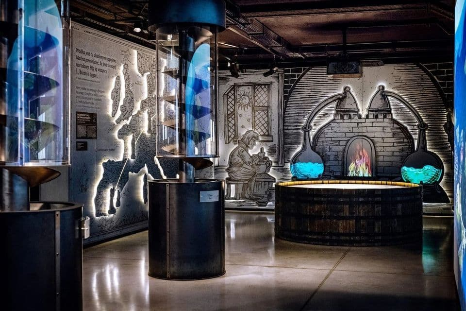 An exhibition room in a modern museum displaying distillation equipment with backlit illustrations of a laboratory on the wall.