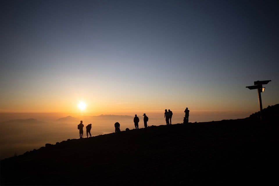 Un gruppo WeRoad in silhouette su una montagna, che osserva l'alba su un mare di nuvole.