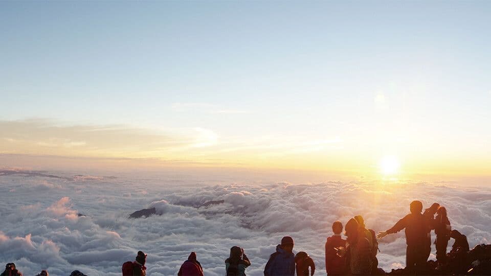 Un gruppo WeRoad in silhouette sulla cima di una montagna, che ammira l'alba sopra un mare di nuvole.