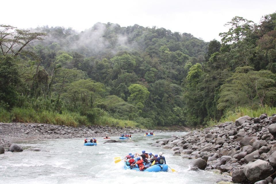 Un voyage de groupe WeRoad en rafting en eaux vives, dans des bateaux pneumatiques bleus, sur une rivière entourée d'une jungle dense et brumeuse.