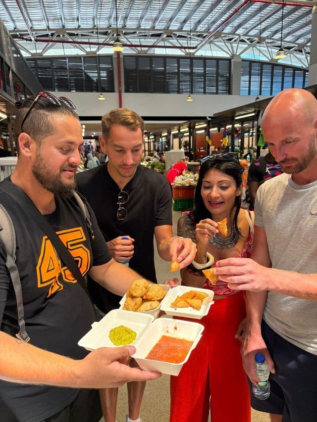Un voyage en groupe WeRoad partage des beignets frits et des sauces d'accompagnement de boîtes à emporter, debout dans un marché couvert animé.