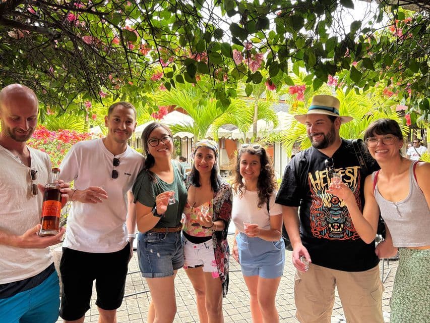 Un voyage de groupe WeRoad de sept personnes souriantes et tenant de petits verres pour une dégustation sous une canopée de fleurs roses.