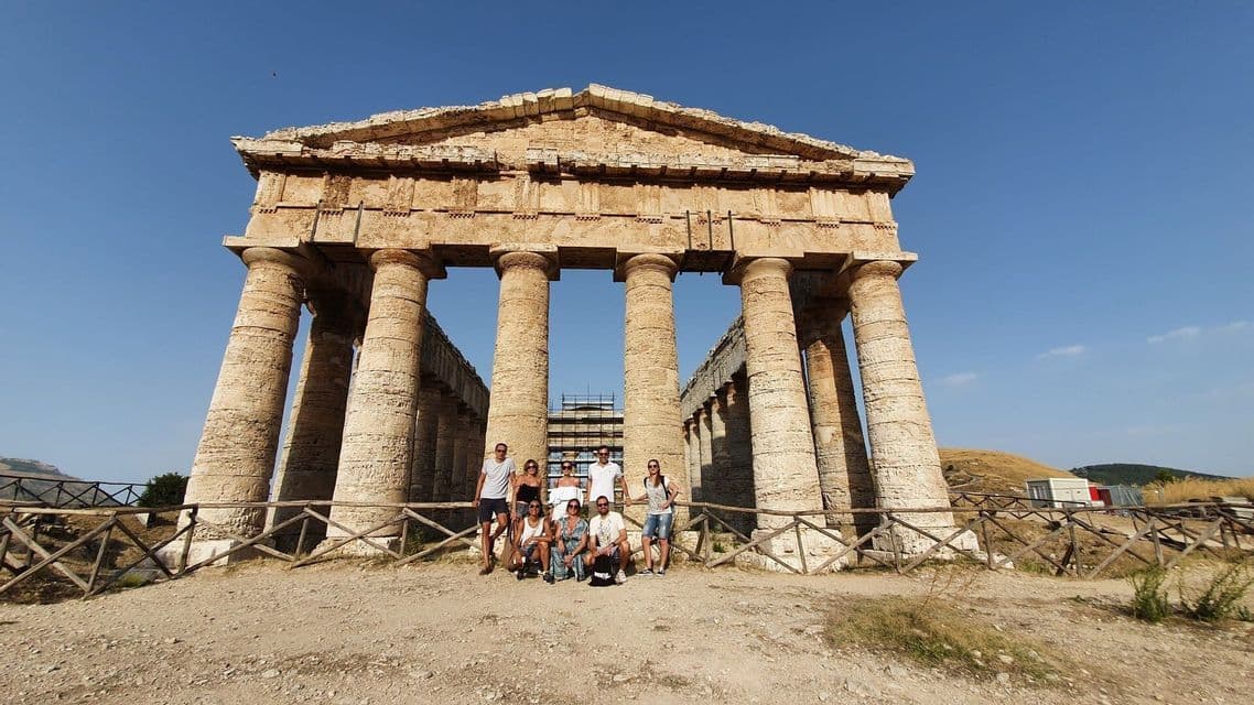 Un gruppo WeRoad in viaggio si fa fotografare davanti a un grande e antico tempio di pietra con colonne imponenti sotto un cielo limpido.