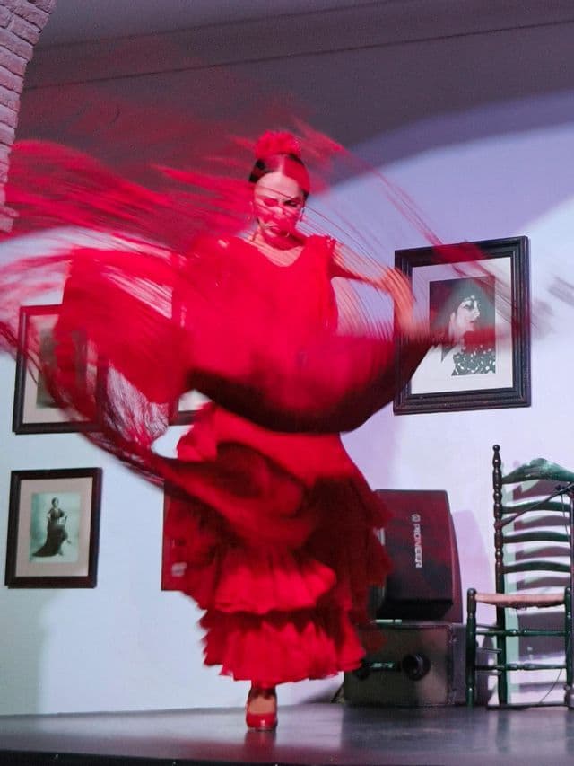 Una ballerina di flamenco in abito e scialle rossi si esibisce sul palco, con il movimento che crea una vibrante scia rossa.