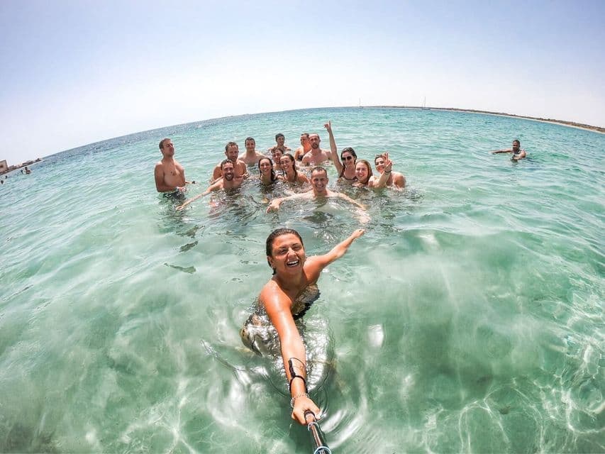 Una donna scatta un selfie del suo viaggio di gruppo WeRoad mentre nuotano insieme in acque cristalline turchesi in una giornata di sole.