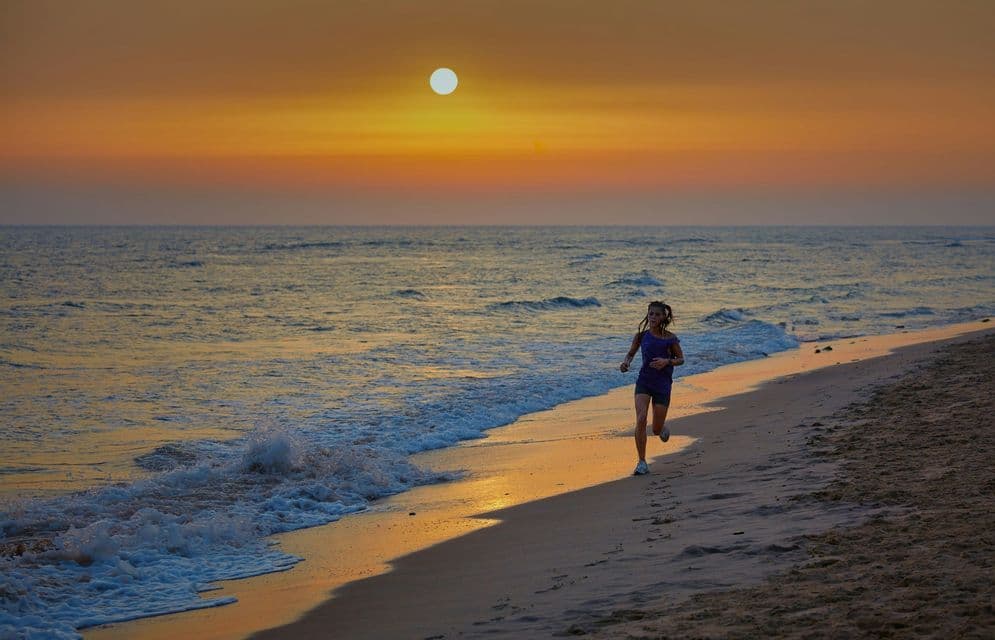 Un giovane corre lungo la battigia sabbiosa di una spiaggia mentre il sole tramonta sull'oceano.