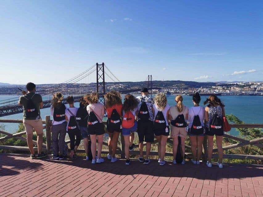 Un gruppo WeRoad, visto di spalle, ammira da un punto panoramico un grande ponte sospeso sull'acqua.