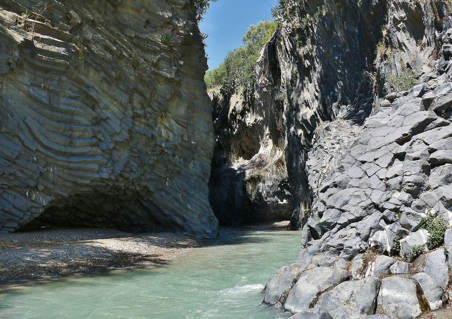 Un fiume con acqua turchese si snoda attraverso una gola stretta con alte pareti di roccia vulcanica stratificata e fratturata.