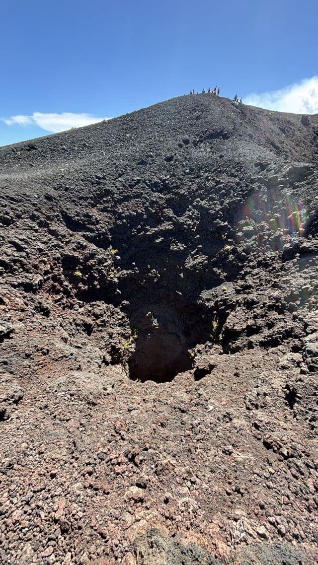 Una vista dal basso di una collina rocciosa e vulcanica, con un gruppo WeRoad in piedi sulla cima contro un cielo azzurro.