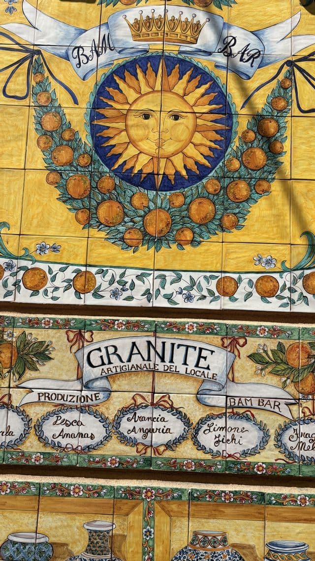 Un murale in piastrelle di ceramica, colorato e dipinto a mano per il 'Bam Bar', raffigurante un sole sorridente circondato da ghirlande di arance.
