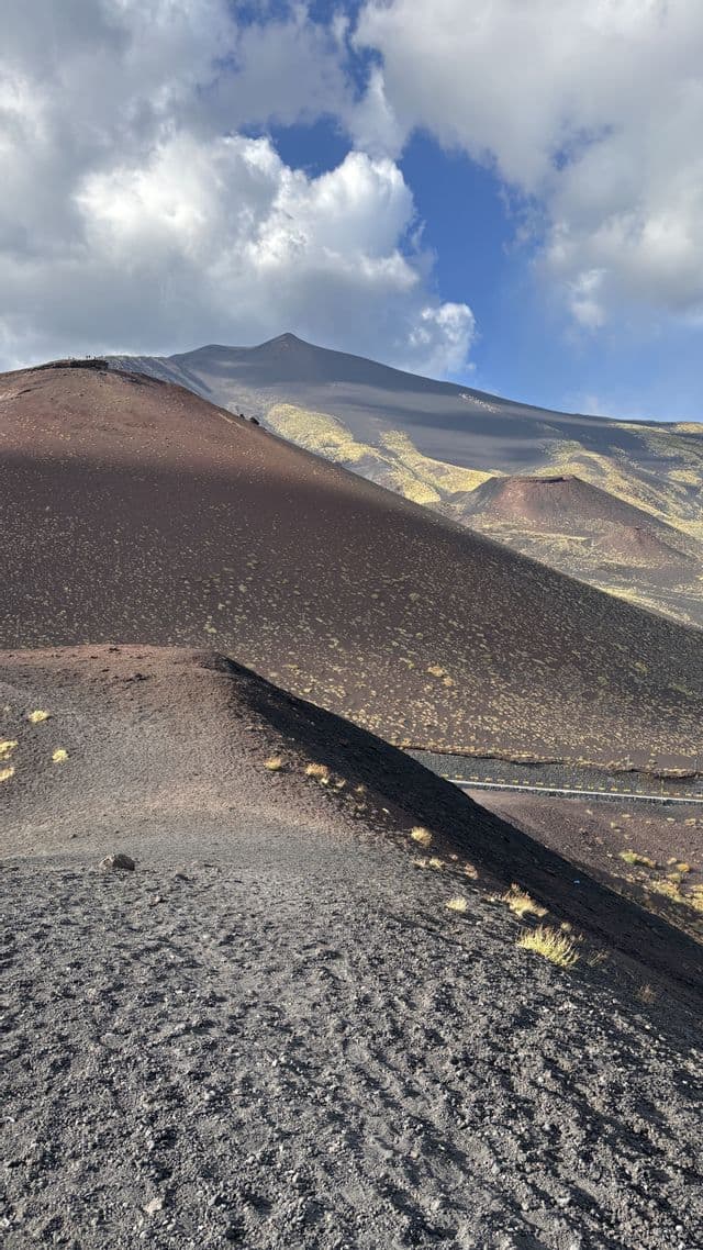 Un viaggio di gruppo WeRoad fa trekking sulle pendici di un paesaggio vulcanico costellato di crateri sotto un cielo parzialmente nuvoloso.