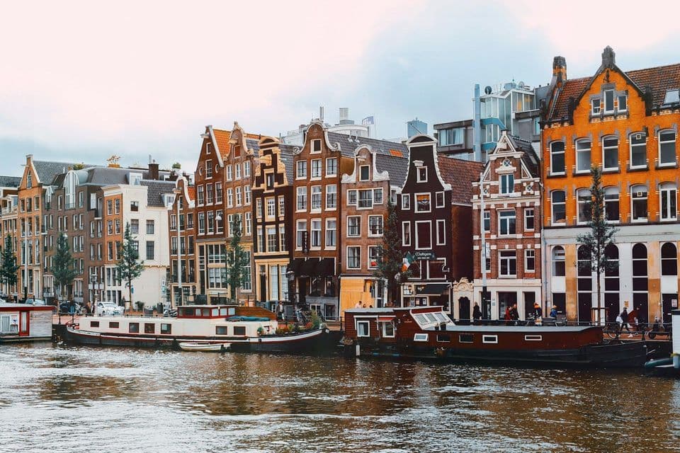 Traditional gabled houses and houseboats moored along a city canal under a cloudy sky.