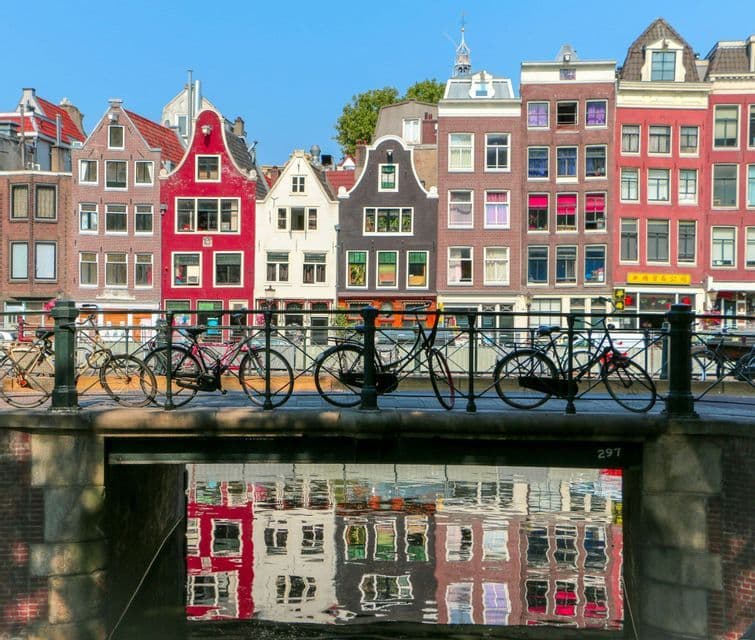 Colorful gabled houses reflected in a canal, with bicycles parked along a bridge in the foreground.