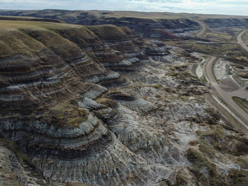 Veduta aerea di un vasto paesaggio di calanchi, con formazioni rocciose erose e stratificate lungo una strada tortuosa in una valle.