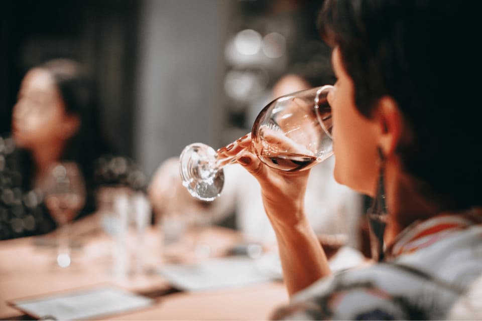Primo piano di una persona durante un viaggio di gruppo WeRoad che beve vino rosso da un bicchiere a tavola.