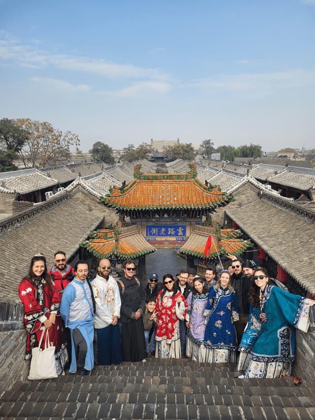 Un viaggio di gruppo WeRoad posa su gradini di pietra in costumi tradizionali asiatici, con i tetti di una città storica sullo sfondo.