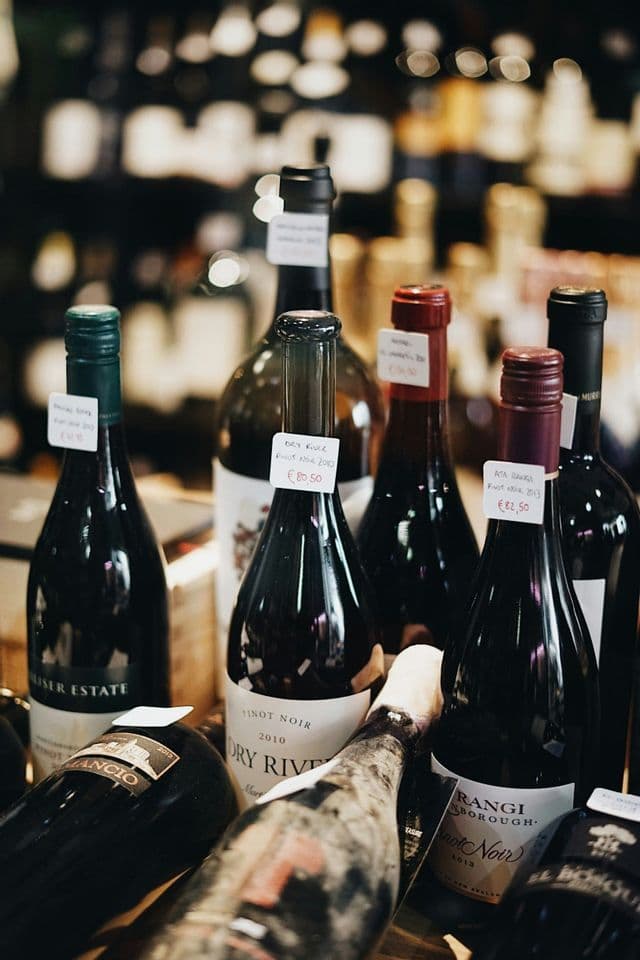 Gros plan sur plusieurs bouteilles de vin rouge avec étiquettes de prix affichées dans une boutique, d'autres bouteilles étant floues en arrière-plan.