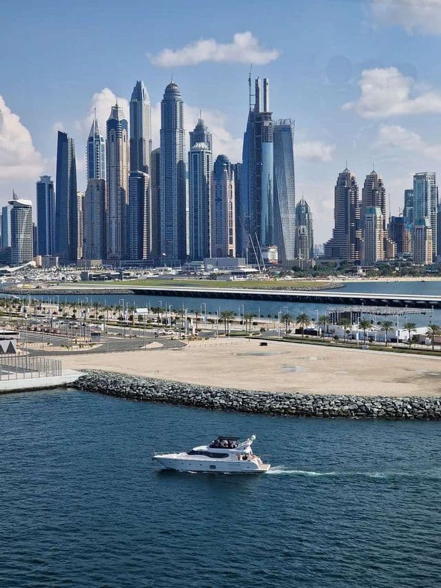 Eine weiße Motoryacht kreuzt auf blauem Wasser, im Hintergrund eine moderne Skyline mit vielen hohen Wolkenkratzern.