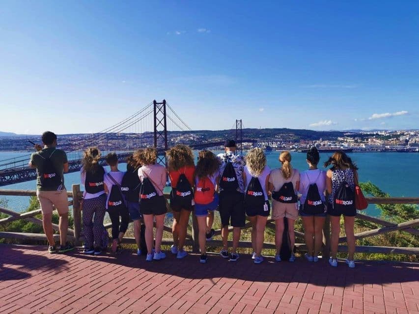 Eine WeRoad-Gruppe von hinten, von einem Aussichtspunkt aus auf eine große Hängebrücke über einem Gewässer blickend.