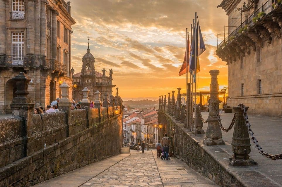 Eine historische Kopfsteinpflasterstraße bei Sonnenuntergang, mit bergab gehenden Menschen und anderen, die links auf einer Terrasse sitzen.