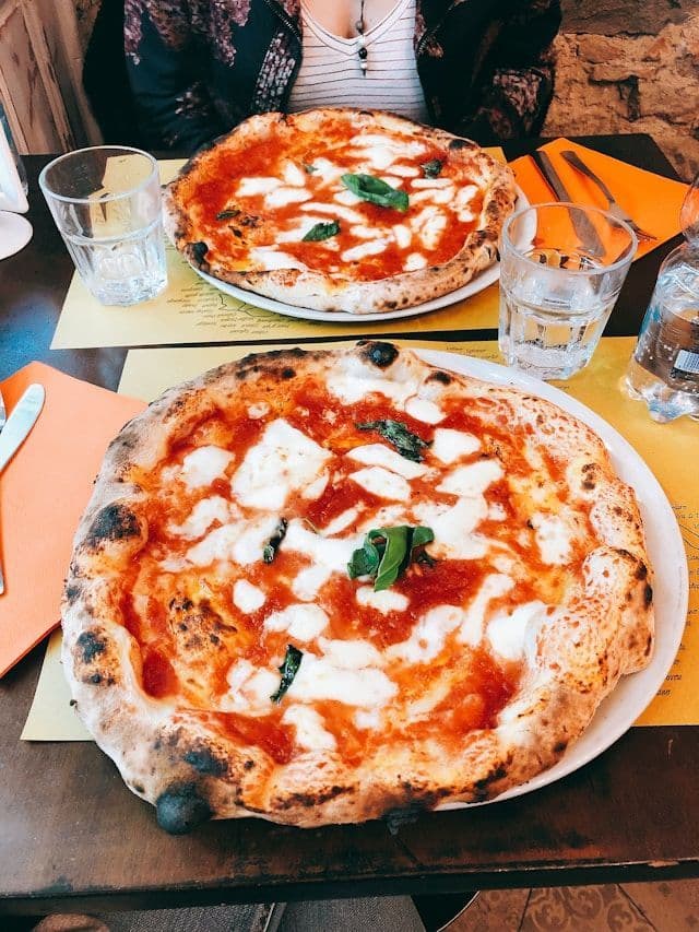 Two Neapolitan margherita pizzas with fresh mozzarella and basil on a restaurant table.