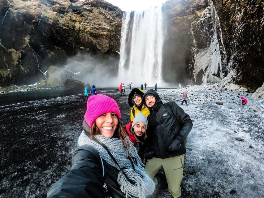 Un grupo de WeRoad de cuatro personas se toma una selfie frente a una gran cascada en una orilla nevada y helada.