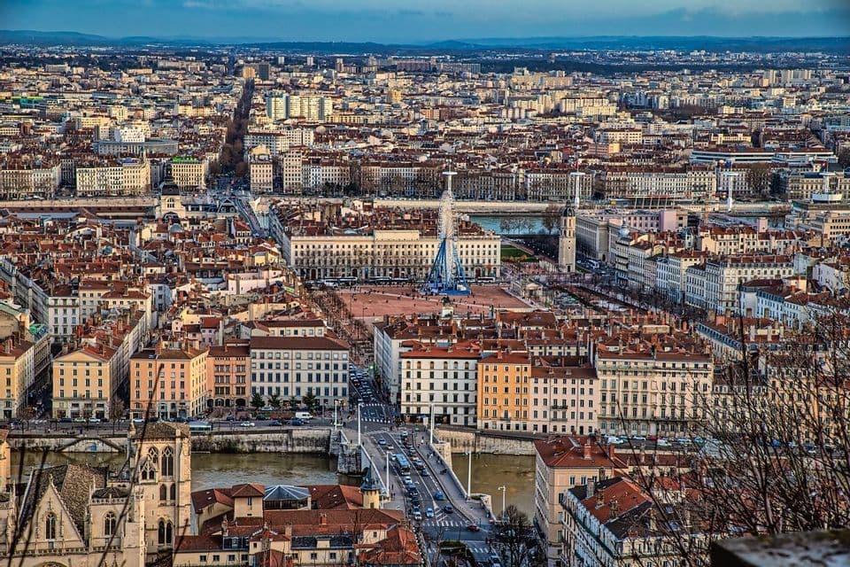 Un vasto paesaggio urbano visto dall'alto, con un fiume, un ponte e un'ampia piazza centrale con una ruota panoramica.