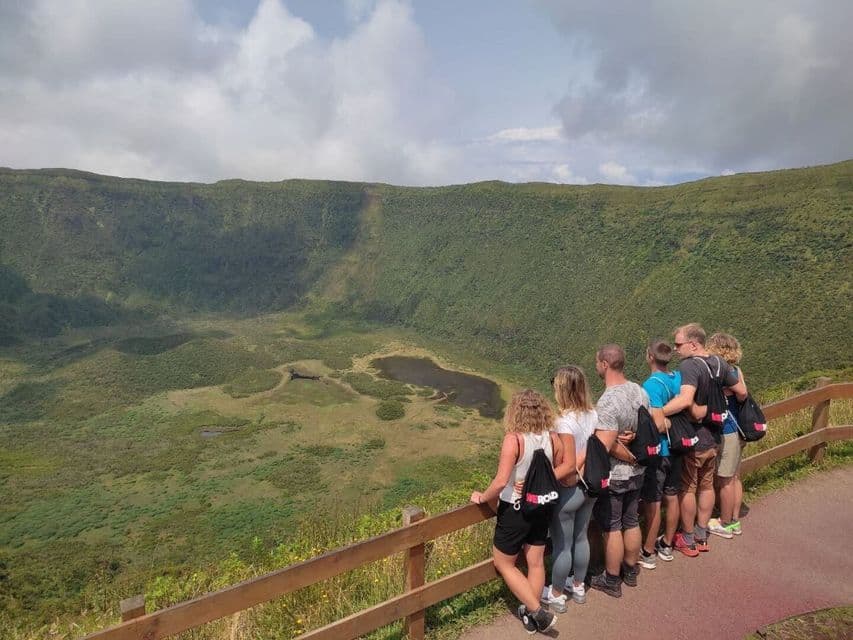 Un gruppo WeRoad si affaccia da un punto panoramico, dietro una staccionata in legno, su un grande cratere vulcanico verde con un lago.