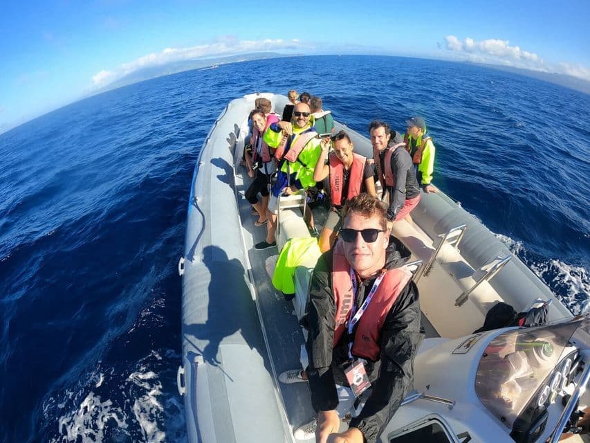 A WeRoad group trip wearing life jackets takes a selfie on a rigid inflatable boat sailing on the open blue sea.