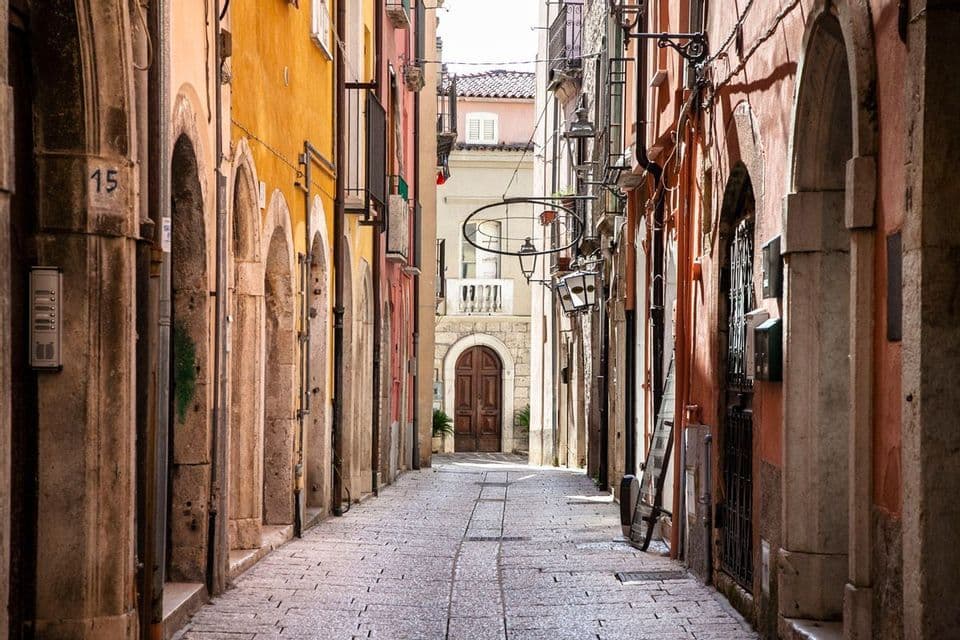 Uno stretto vicolo lastricato in pietra, che si snoda tra colorati edifici storici con archi in pietra.