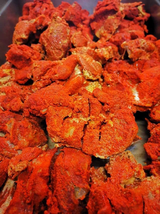 Un primo piano di pezzi di carne cruda generosamente cosparsi di un vivace mix di spezie rosse in polvere.