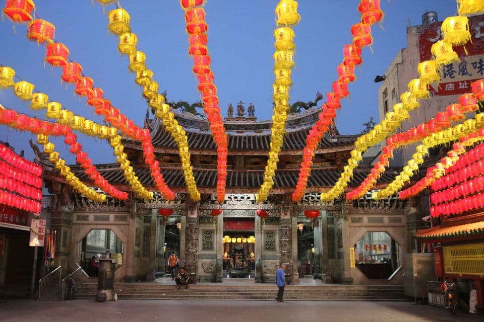 Reihen beleuchteter roter und gelber Papierlaternen hängen in der Dämmerung vor einem verzierten asiatischen Tempel.