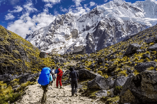 Un viaje en grupo de WeRoad con excursionistas mochileros subiendo por un sendero rocoso hacia una enorme montaña nevada.