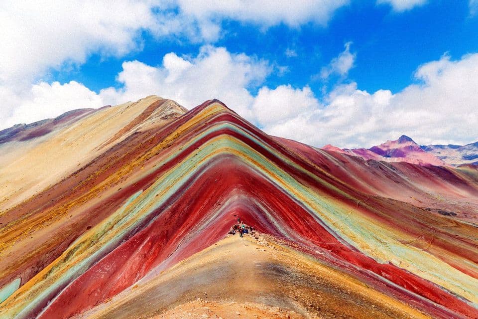 Un viaje en grupo de WeRoad se encuentra en la cresta de una montaña con rayas minerales coloridas bajo un cielo azul nublado.