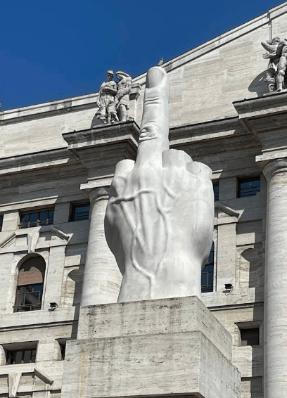 Una gran escultura de mármol blanco de una mano con el dedo corazón extendido, situada frente a un edificio clásico.