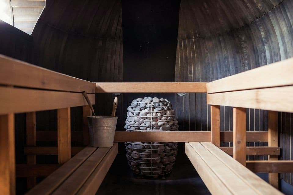 Vista dal basso dell'interno di una sauna a botte in legno con panche, una stufa centrale in pietra e un secchio.