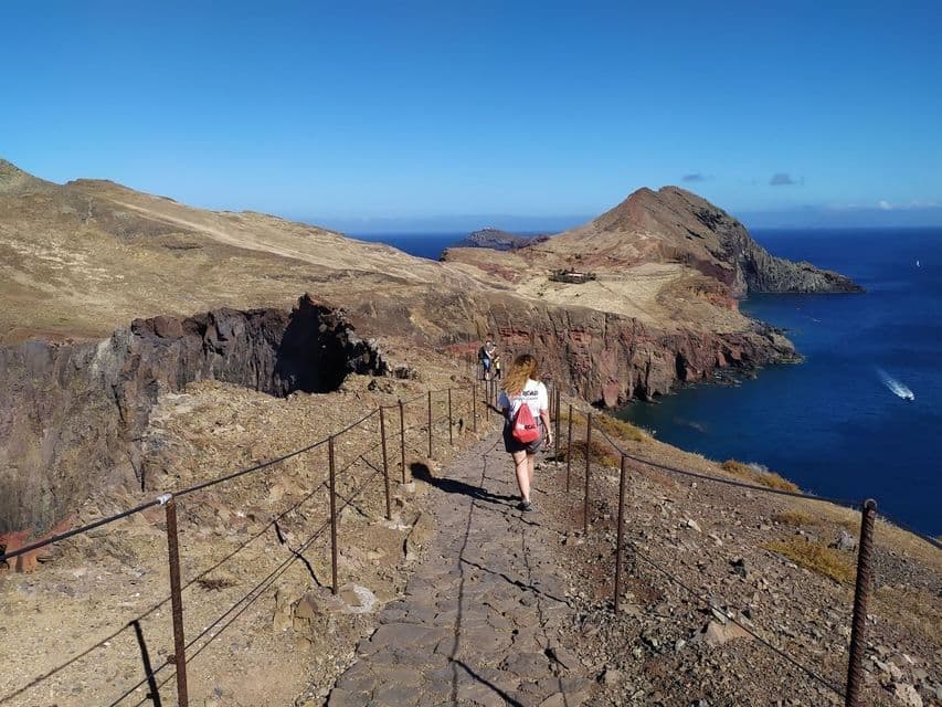 Une personne d'un voyage de groupe WeRoad randonnant le long d'un sentier côtier étroit sur une falaise surplombant l'océan par une journée ensoleillée.