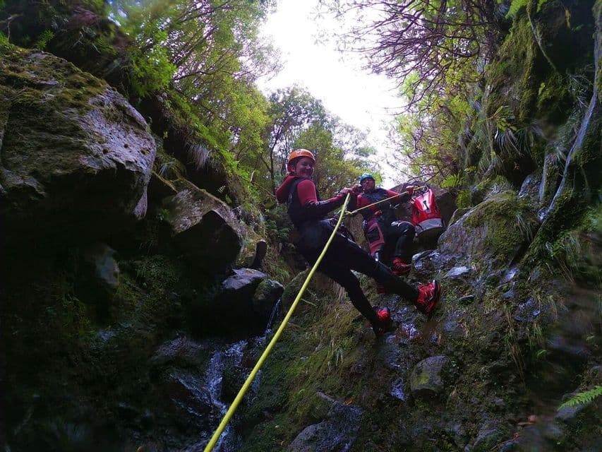 Due persone di un viaggio di gruppo WeRoad, con caschi e mute, fanno canyoning lungo una parete rocciosa muschiosa in un canyon.
