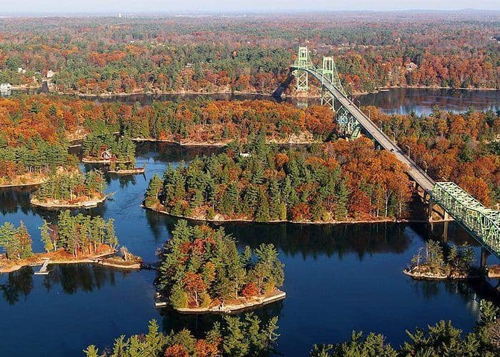 Una vista aerea di un lungo ponte verde che attraversa un fiume costellato da numerose piccole isole coperte da colorate foreste autunnali.