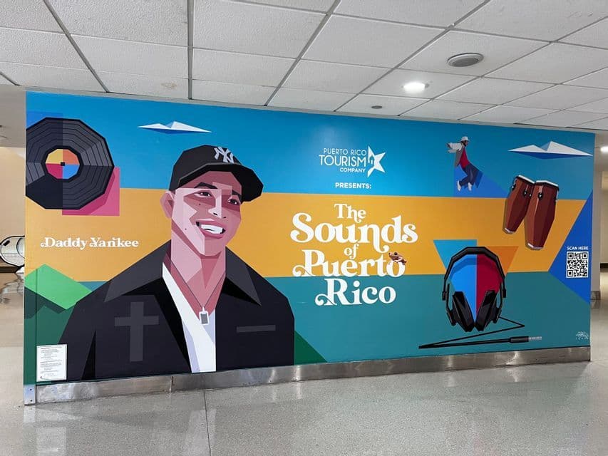 Un colorido mural de pared promocionando 'Los Sonidos de Puerto Rico', con una ilustración estilizada del artista Daddy Yankee dentro de un edificio.