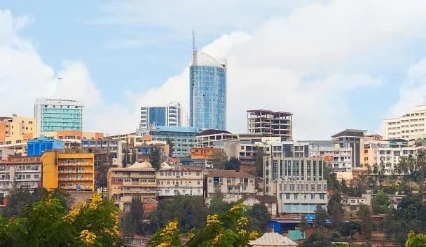 Un paysage urbain avec des gratte-ciel modernes et des bâtiments plus petits construits à flanc de colline sous un ciel partiellement nuageux.