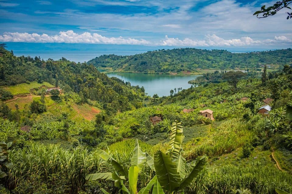 Vue étendue sur un lac entouré de collines verdoyantes parsemées de maisons et de fermes, sous un ciel bleu partiellement nuageux.