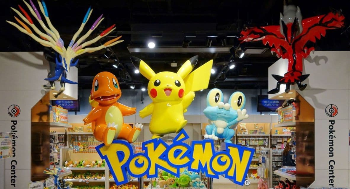 Grandi statue di Pikachu, Charmander e Froakie sopra il logo Pokémon all'ingresso di un negozio Pokémon Center.