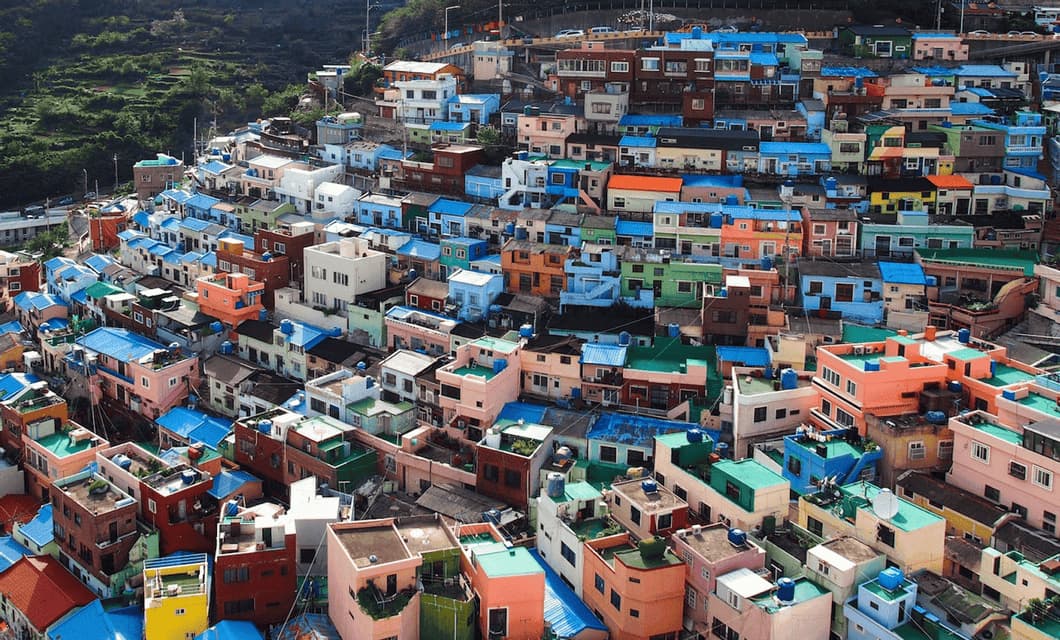 Case colorate con tetti blu brillanti sono addossate strettamente su un ripido versante verde in un villaggio denso.